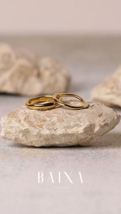 two gold wedding rings sitting on top of a rock