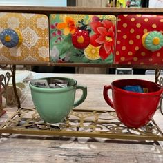 three colorful cups are sitting on a metal rack with flowers painted on it and one has a cup holder in the middle