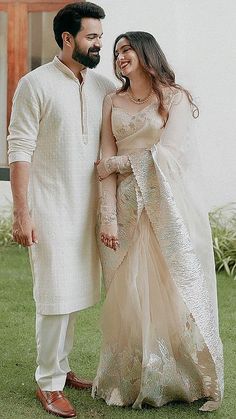 a man and woman standing next to each other in front of a white building with grass