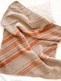 an orange and white knitted blanket laying on top of a bed next to a pillow