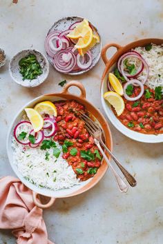 two bowls filled with rice, beans and vegetables next to lemon wedges on a table