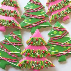 decorated christmas tree cookies sitting on top of a white table next to green and pink trees