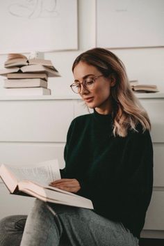 a woman sitting on a chair reading a book in front of a stack of books