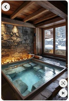 an indoor hot tub with candles in the middle and stone walls around it, next to a window