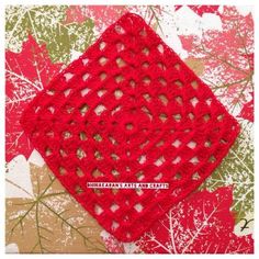 a red crocheted square sitting on top of a leaf covered tablecloth next to a