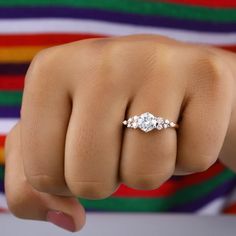 a woman's hand with a three stone ring on her finger, in front of a colorful striped shirt