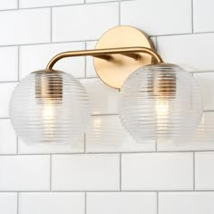 two light bathroom fixture with white tiles on the wall behind it and gold metal fixtures