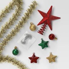 various christmas ornaments and decorations on a white surface with gold tinsel, red and green baubles