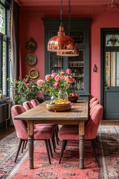 a dining room with pink chairs and a wooden table surrounded by potted plants on top of a rug