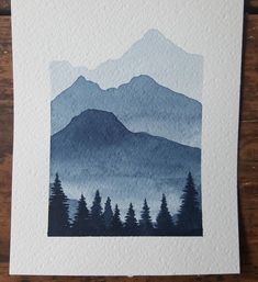 a watercolor painting of mountains and trees on white paper with blue hues in the background