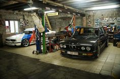 two cars parked in a garage next to each other and one is being worked on