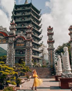 a woman in a yellow dress is standing on some steps near statues and pagodas