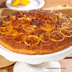 a cake with orange slices on it sitting on a white platter next to some plates