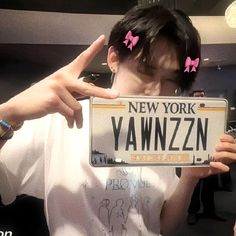 a man holding up a new york license plate with pink bows on his head and fingers