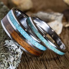 two rings with wood and turquoise inlays are sitting on top of a rock