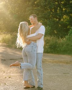 a man and woman standing next to each other on a dirt road with trees in the background