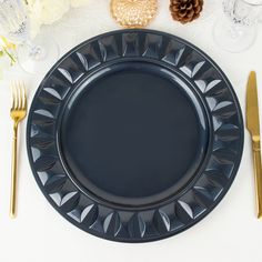 a black plate with gold forks and knifes on a white table cloth next to some pine cones