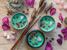 two bowls filled with green liquid surrounded by purple flowers and other items on a wooden table