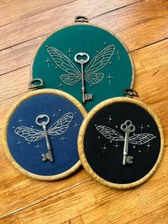 three embroidery hoops with key and dragon designs on them sitting on a wooden floor