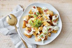 a white plate topped with potatoes covered in cheese and bacon next to a gold spoon