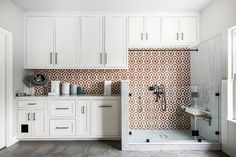 a bathroom with white cabinets and an orange patterned tile backsplash on the wall