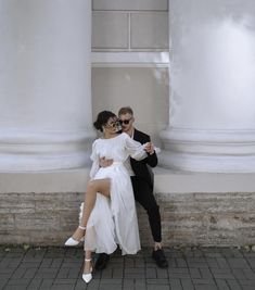 a man and woman pose for a photo in front of some white pillars with their arms around each other