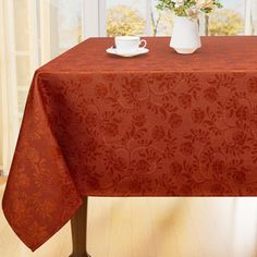 a red table cloth with flowers in vases on it and an empty coffee cup at the end