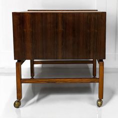 a wooden cabinet sitting on wheels against a white wall