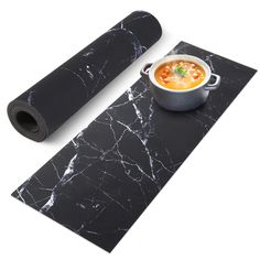 a black mat with a bowl of soup on it next to a roll of yoga mats