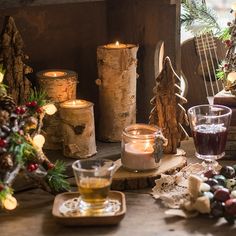 candles and other decorations on a table in front of a window with christmas tree branches