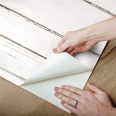 two hands holding an envelope over a piece of paper on top of a wooden table