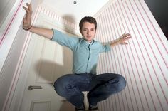 a man sitting on top of a chair in front of a wall with red stripes