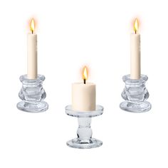 three lit candles sitting on top of clear glass holders in front of a white background