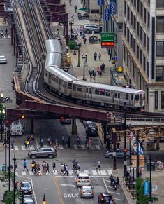 a silver train traveling over a bridge next to tall buildings and traffic lights on a city street