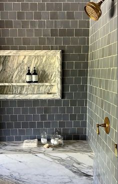 a bathroom with marble counter tops and gray tiles on the walls, along with gold faucets