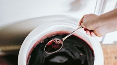 a person holding a spoon over a bowl filled with red liquid