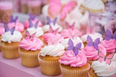 cupcakes with pink frosting and purple butterflies on them are sitting on a table