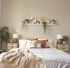 a bed with white sheets, pillows and plants on the headboard in a bedroom