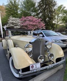 an antique car is parked next to another classic car in a parking lot near some trees