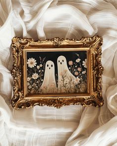 a painting with two ghost faces on it in a gold frame, surrounded by white fabric