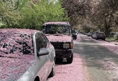 the cars are parked on the side of the road covered in pink flowers and petals