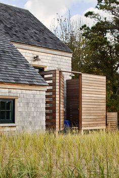 an old brick building with a black roof and wooden shutters on the windows is surrounded by tall grass