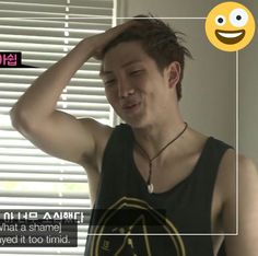 a young man is smiling and holding his head in one hand while wearing a black tank top with an emoticive smiley face on it