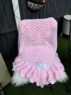 a pink crocheted blanket sitting on top of a metal stand next to a potted plant