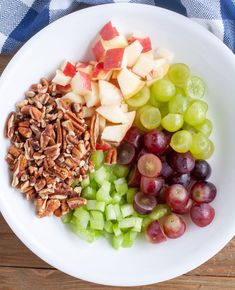 grapes, pecans, and apples are arranged in a white bowl on a wooden table