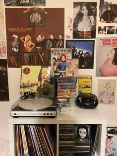 a record player sitting on top of a white shelf filled with dvds and cds next to a wall full of movie posters