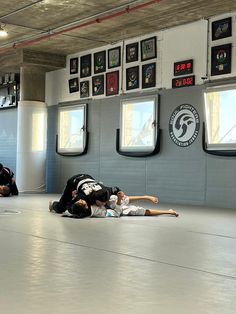 two men are wrestling in a gym with one laying on the floor and another standing