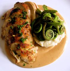 a white plate topped with chicken, mashed potatoes and broccoli covered in gravy