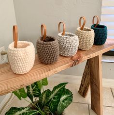 three knitted baskets sitting on top of a wooden table next to a potted plant