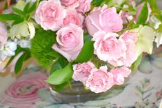 a vase filled with pink and white flowers on top of a floral tablecloth covered table